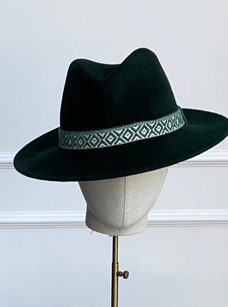 A dark green fedora hat with a patterned band on a display stand. | Sarah Ross Millinery