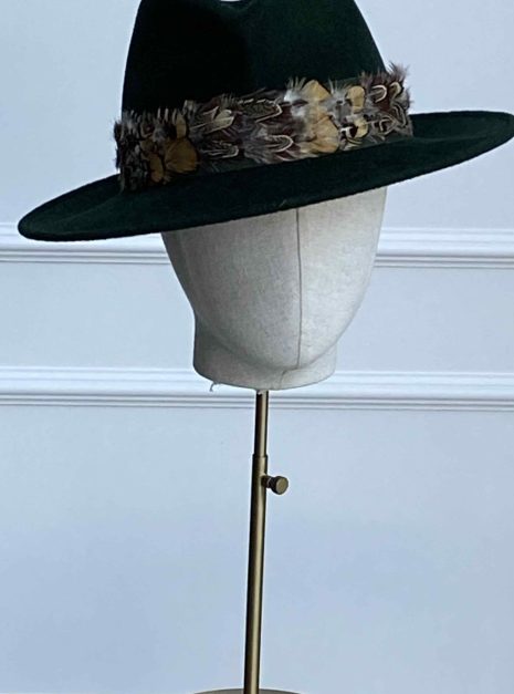A dark green fedora with a feathered band displayed on a mannequin head atop a stand. | Sarah Ross Millinery