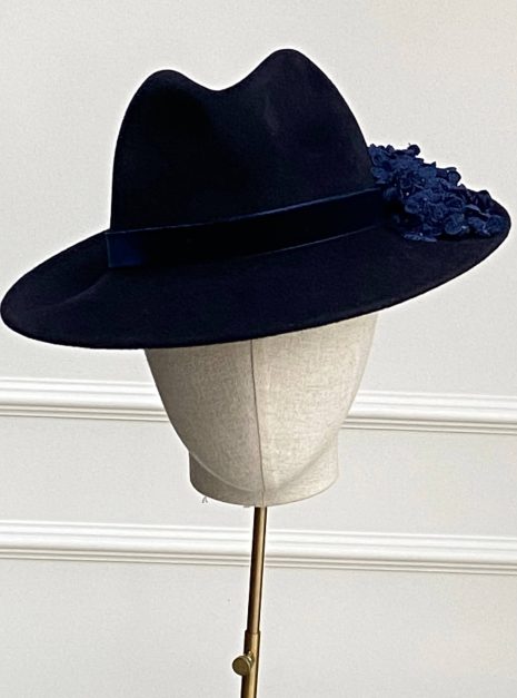 A black hat with a wide brim and dark floral details on the side, displayed on a mannequin head. | Sarah Ross Millinery