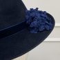 A dark blue felt hat with a wide brim, featuring a navy ribbon and a cluster of blue floral appliques on one side. | Sarah Ross Millinery