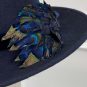 A dark blue hat with a band, featuring decorative blue and green peacock feathers on the side. | Sarah Ross Millinery