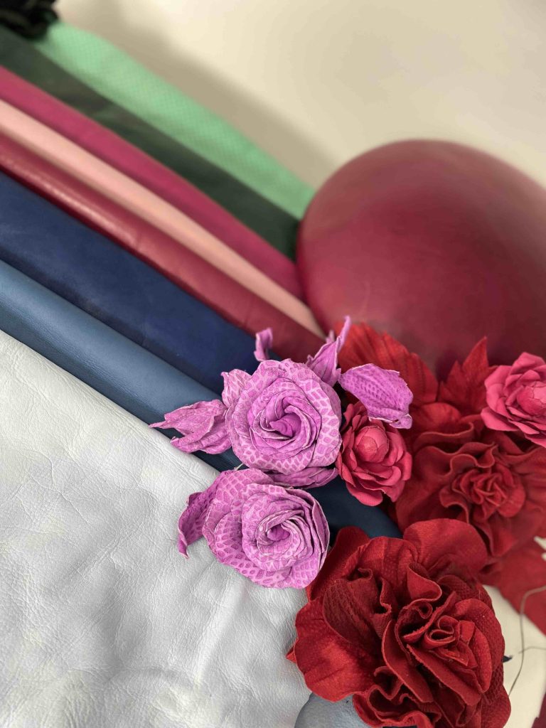 A variety of colorful fabrics are stacked, including pink, red, and green. Pink and red fabric flowers are arranged on top. | Sarah Ross Millinery