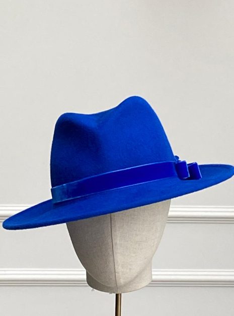 The Galon Fedora in Royal Blue, featuring a velvet headband and bow, elegantly displayed on a stand with a plain background. | Sarah Ross Millinery