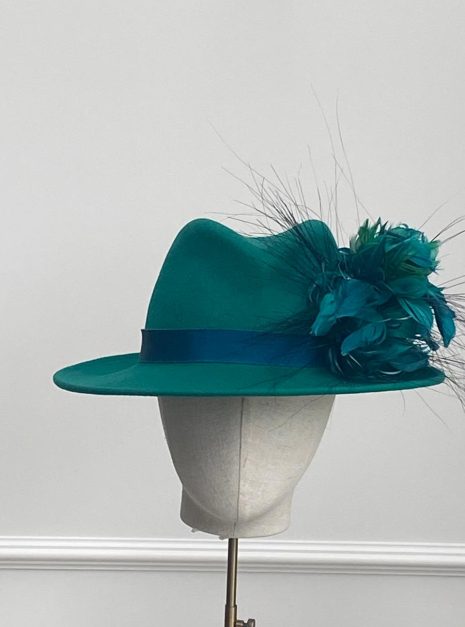 A Classic emerald green fedora with a teal hat ribbon is displayed on a mannequin stand against a neutral background. | Sarah Ross Millinery